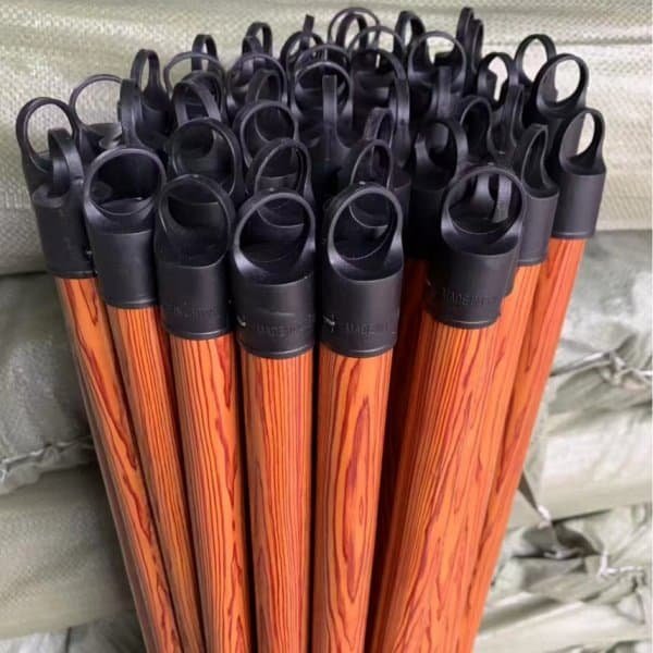 Stacked wooden broom handles with black plastic hanging end caps and wood-grain finish in a warehouse