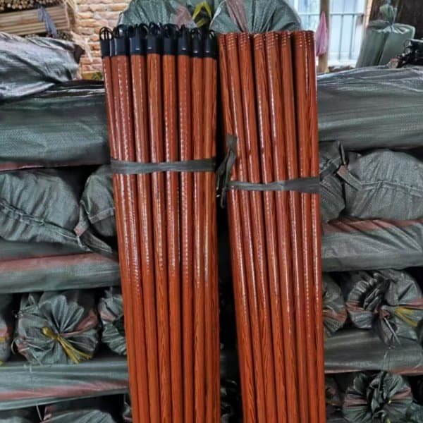 Two bundles of smooth pvc coated wooden broom handles with black caps in a storage warehouse