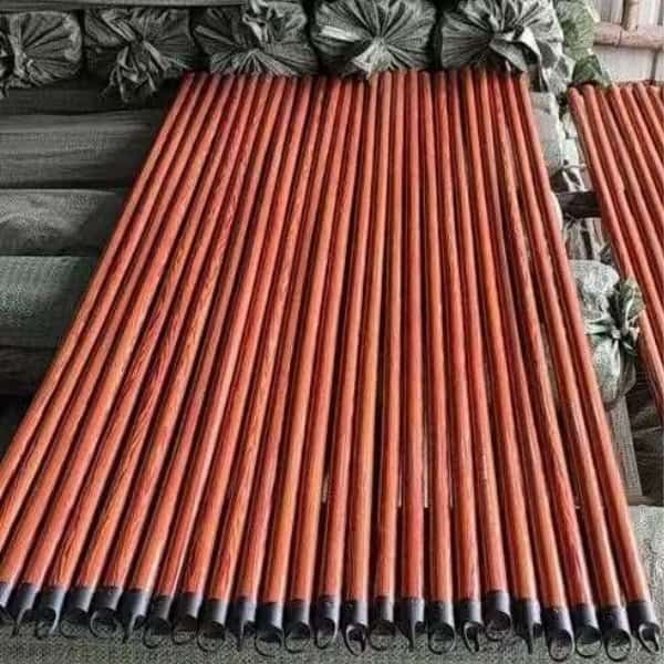 Bundles of reddish-brown wooden broom handles with black hanging caps in a warehouse setting