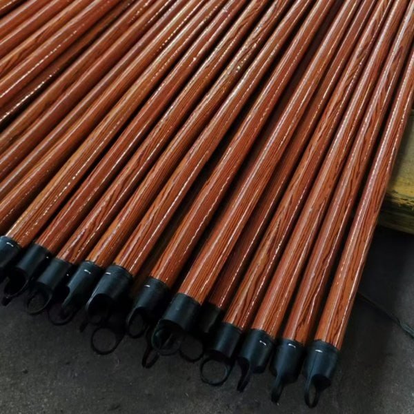 Neatly stacked glossy reddish-brown wooden broom handles with black hanging end caps and clear wood grain