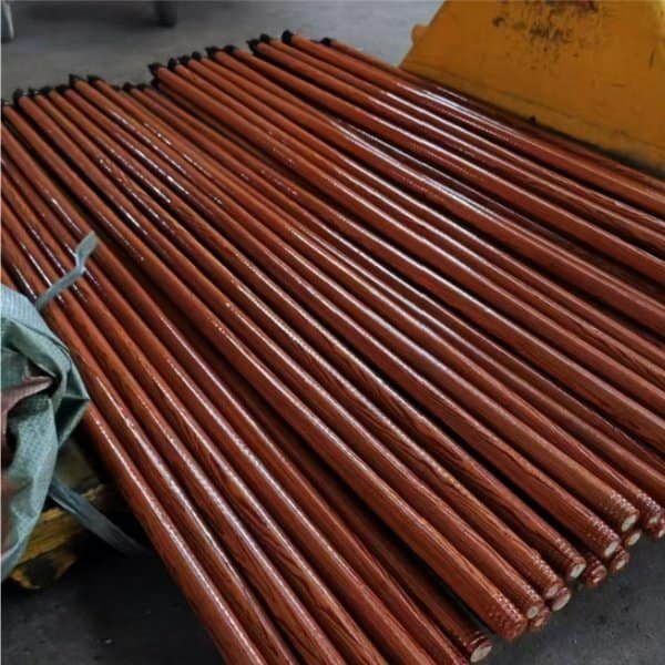 Neatly stacked polished reddish-brown wooden mop handles with clear wood grain.