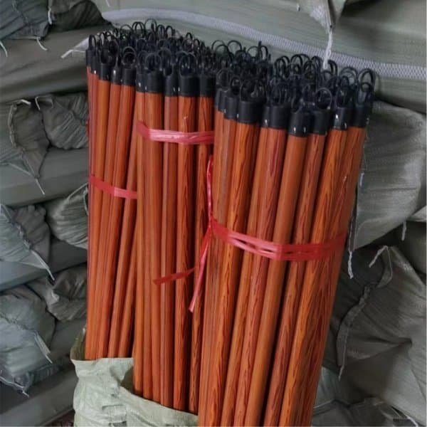Tied bundles of reddish-brown wooden broom handles with black hanging ends stored in a warehouse