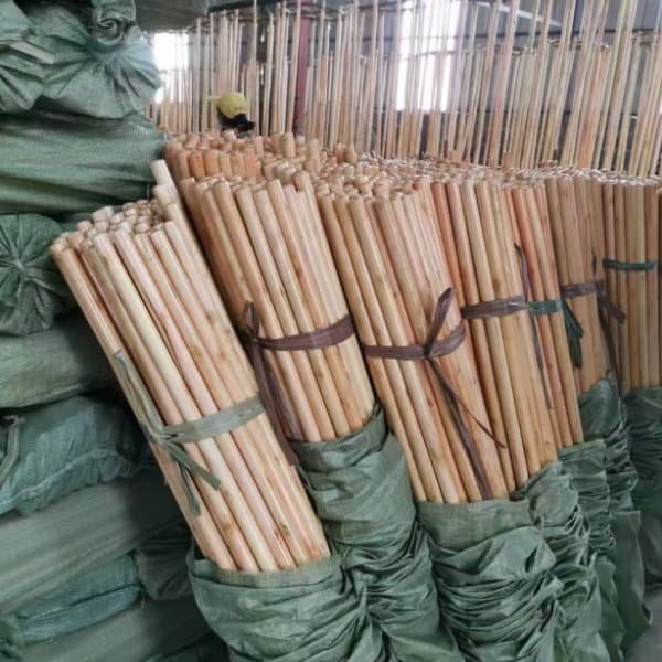 Bundled varnished wooden broom handles stocked in a customized handle equipped garden broom factory