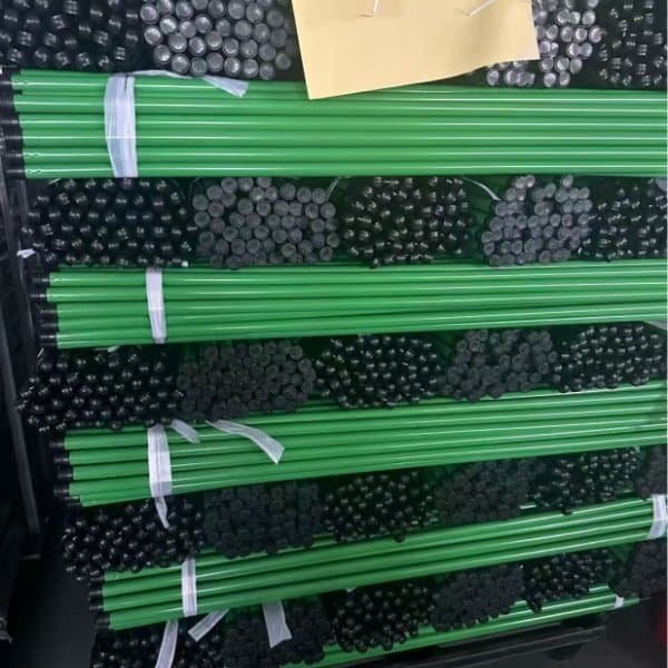 Stacked bundles of green color iron broom sticks with black caps, from reliable wholesale iron stick red broom suppliers for bulk cleaning supply orders.